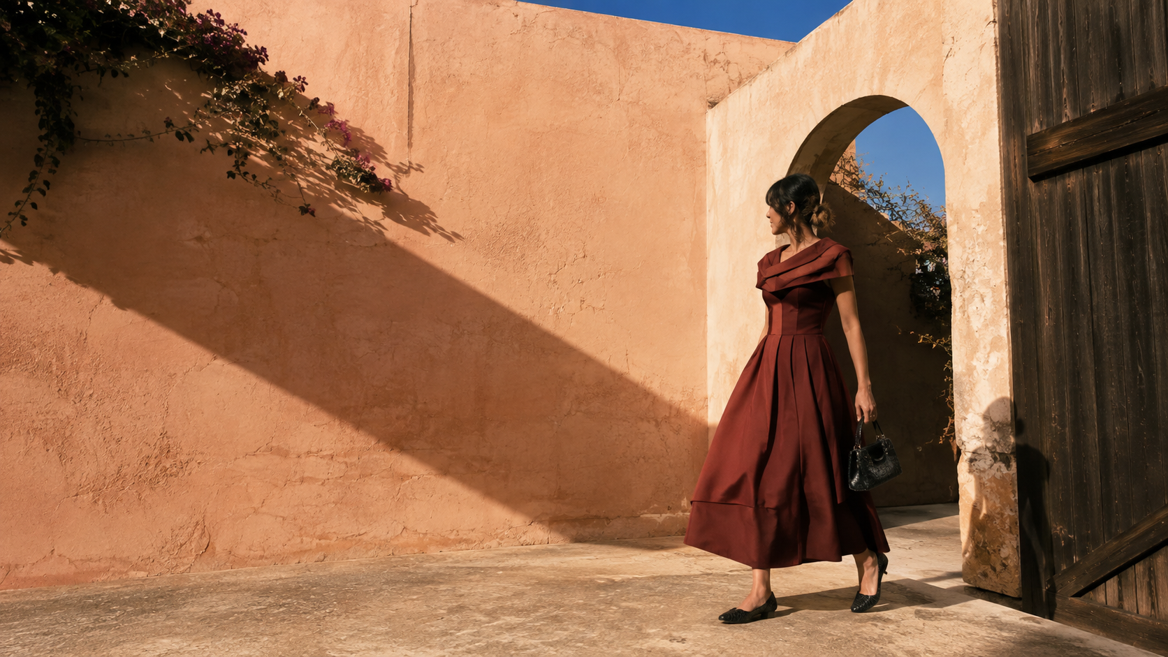 Woman wearing a sculptural oxblood vintage dress in a sunlit courtyard